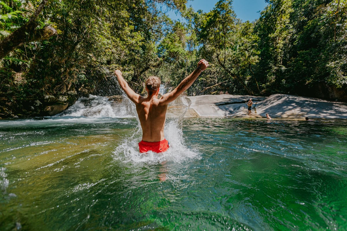 Male with his back turned to camera with is arms extended out in celebration at Josephine Falls