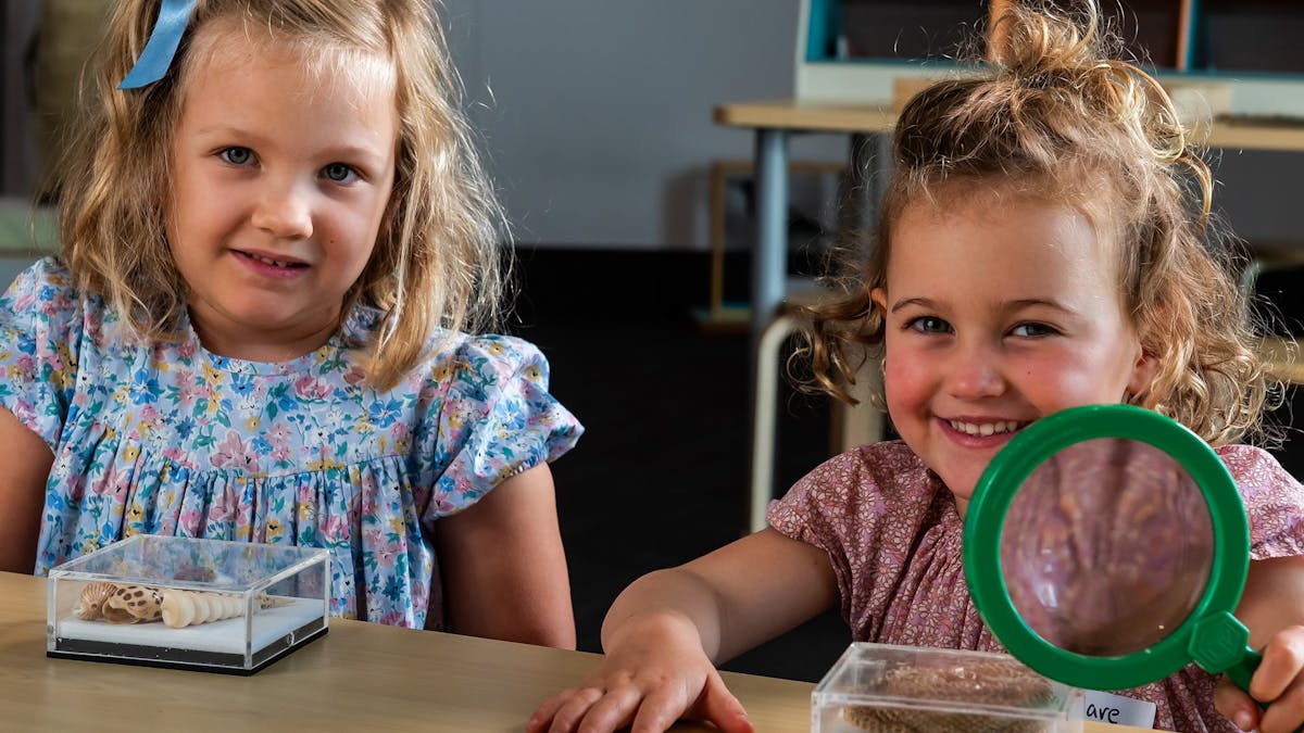 Two children smiling at camera. One holds a magnifiying glass and each have an acrylic seashell box