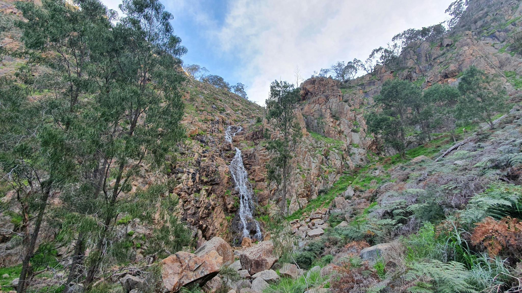 Waterfall over a rock escarpment, rocks, bolders, ferns, gum trees, cliffs, blue sky
