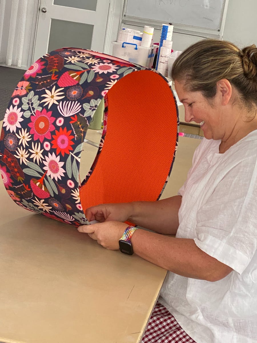 picture of smiling woman making a drum lampshade with orange lining and multicoloured flowers