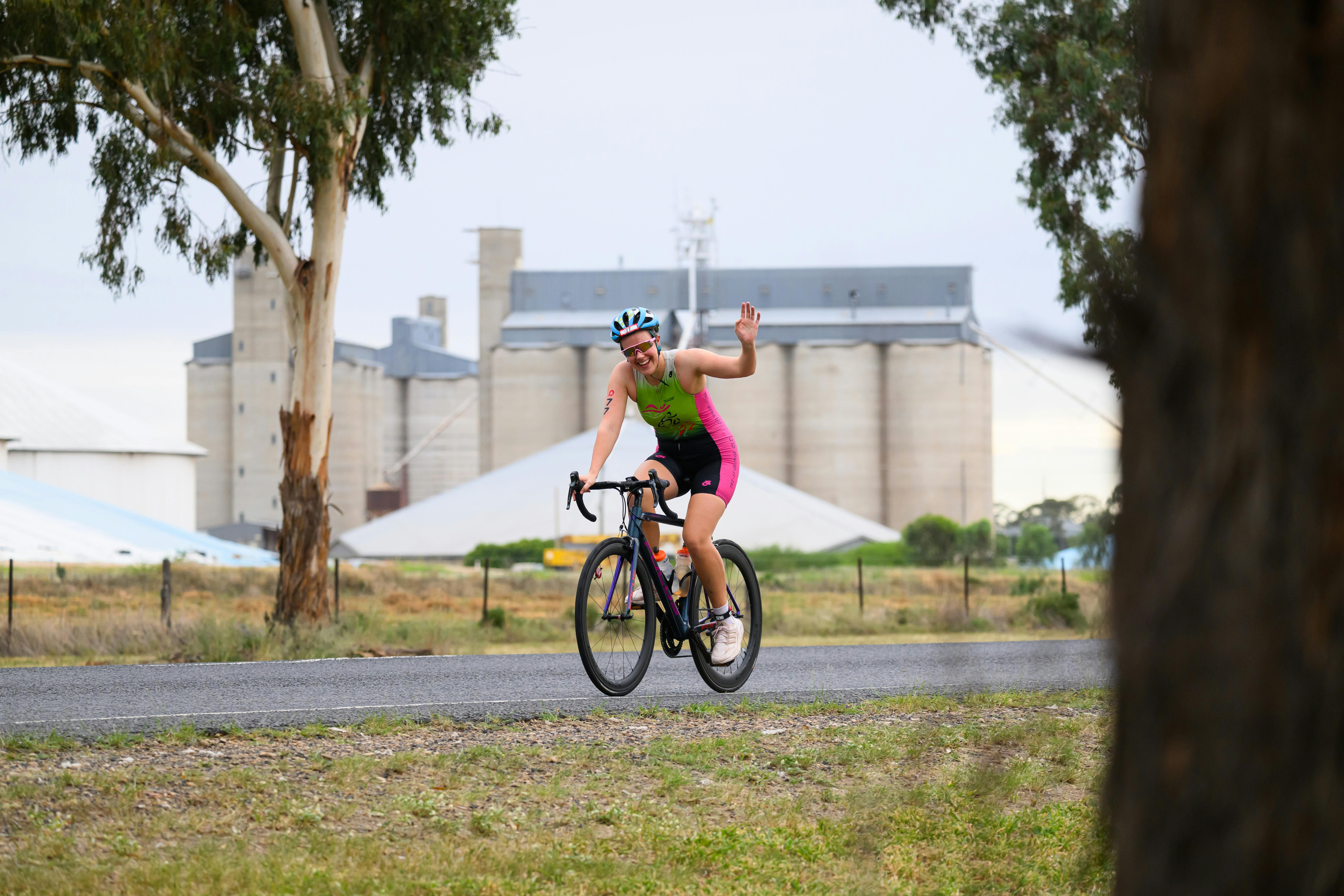 Women cyclist waving with big silos in back ground