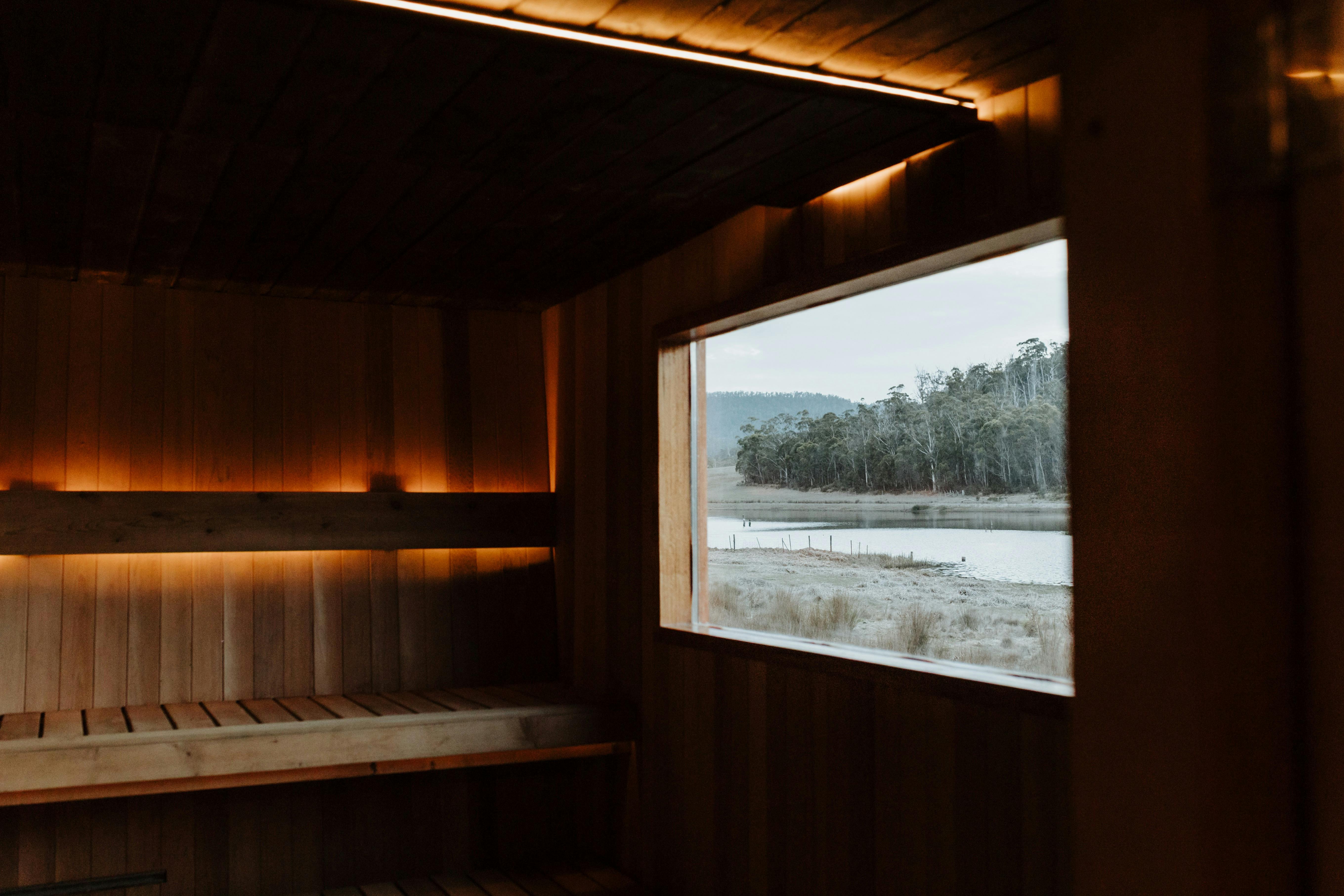 Wood-lined sauna interior with ambient lighting and views of water and bushland.