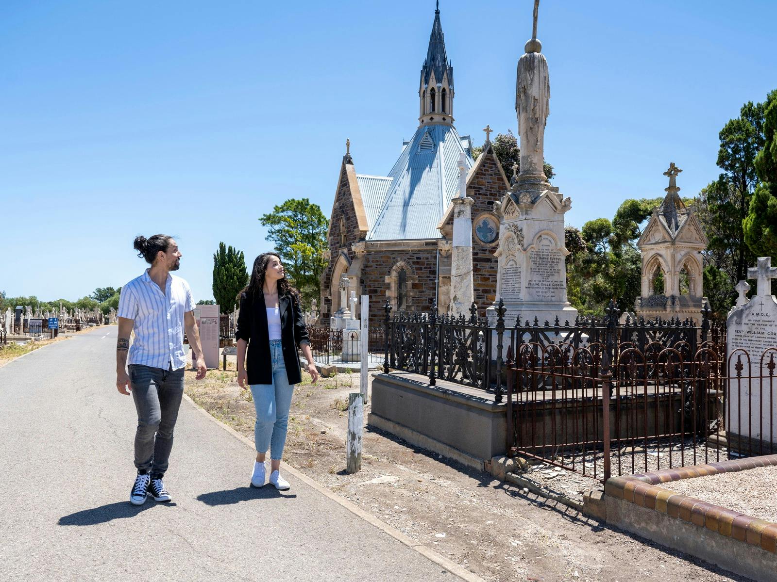 Two young people walking past and looking at a chapel in a cemetery