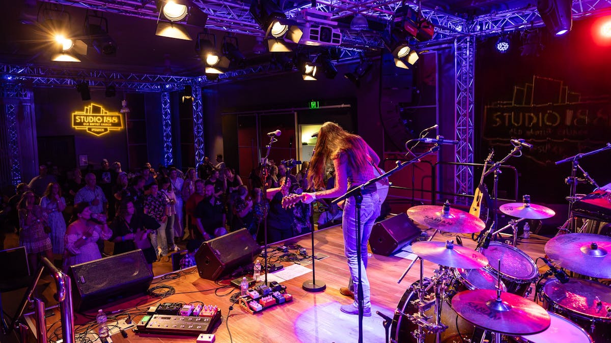 Performer playing guitar on stage to crowd of people