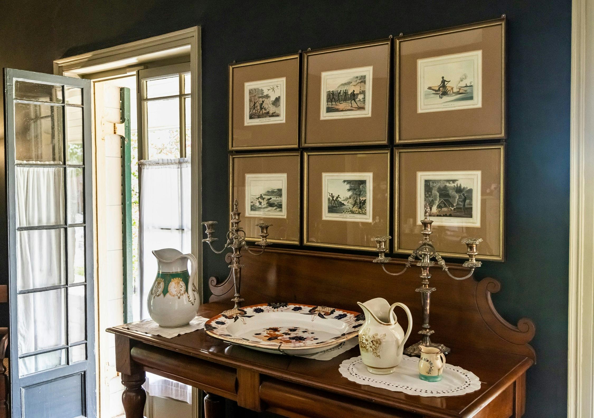 Framed photos on dark wall with side board with historic crockery
