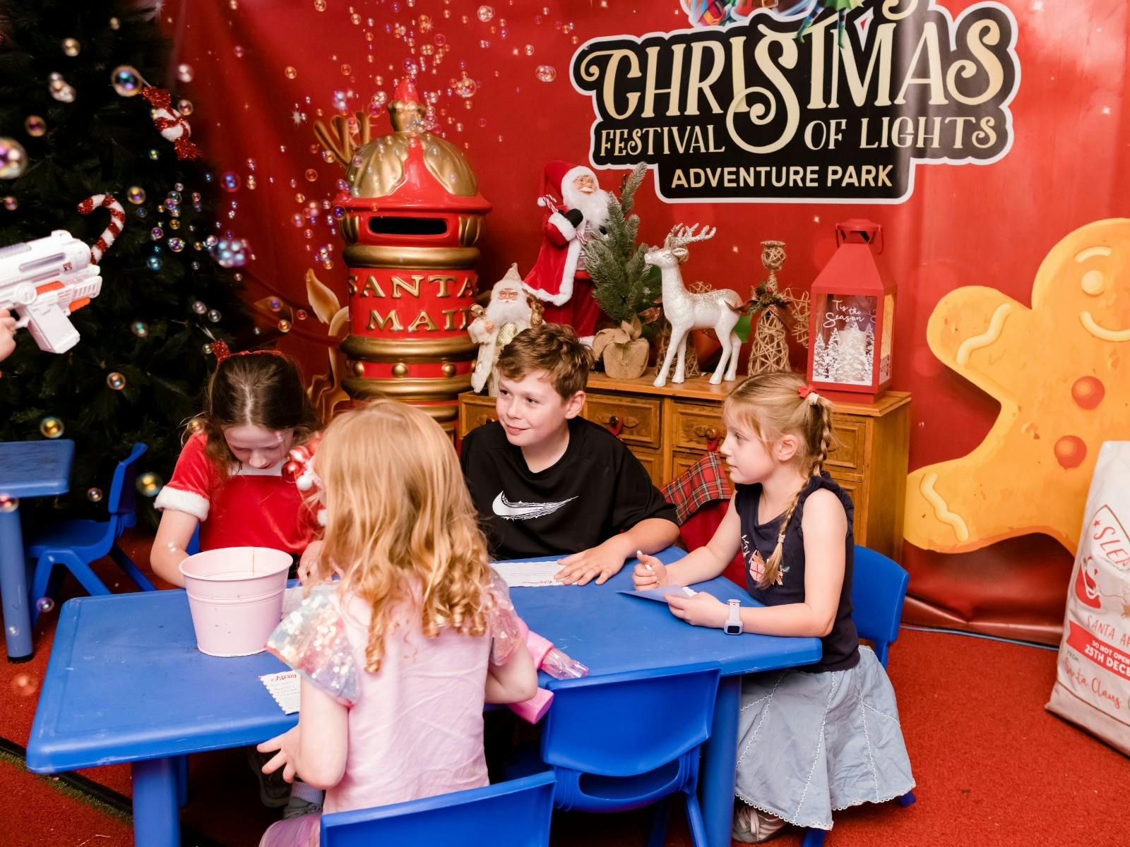 A group of children sat at a blue table, writing letters to Santa