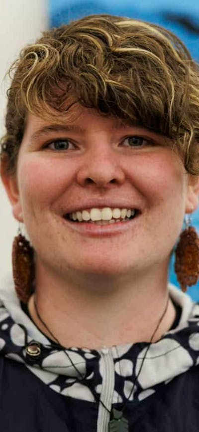 A smiling woman with curly brown hair and large brown earrings, wearing a black jacket.