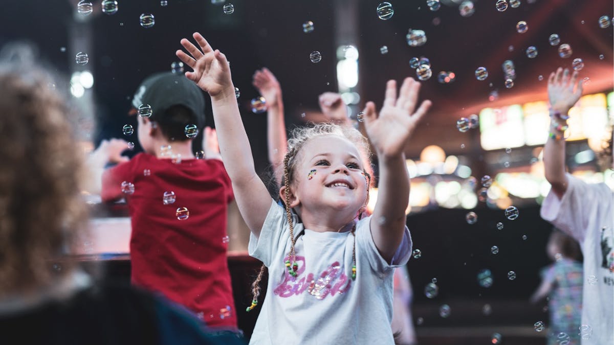 A young girl dancing and smiling while bubbles are floating in the air.