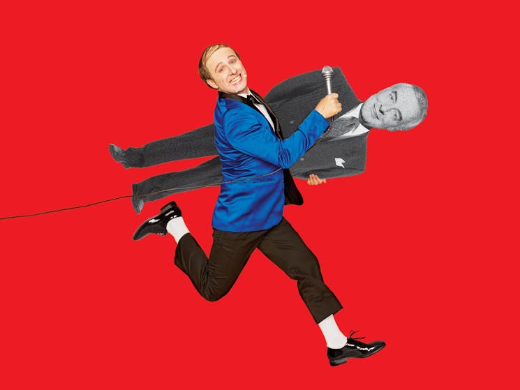 Matthew Whittet, holding a microphone and a cut-out of Gough Whitlam, behind a red background