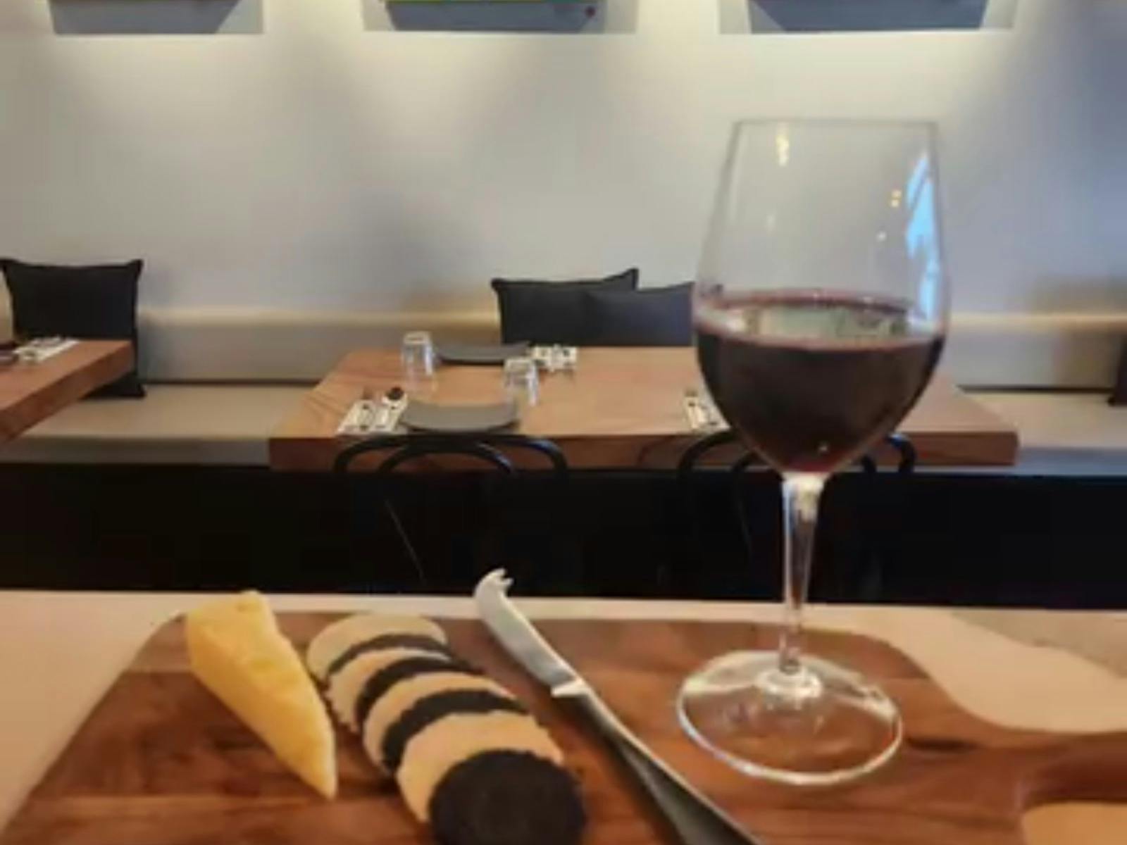 A glass of red wine on a cheese board with cheddar cheese, crackers and a cheese knife.