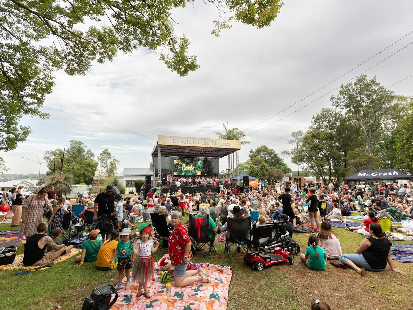 Families sitting on grass with stage