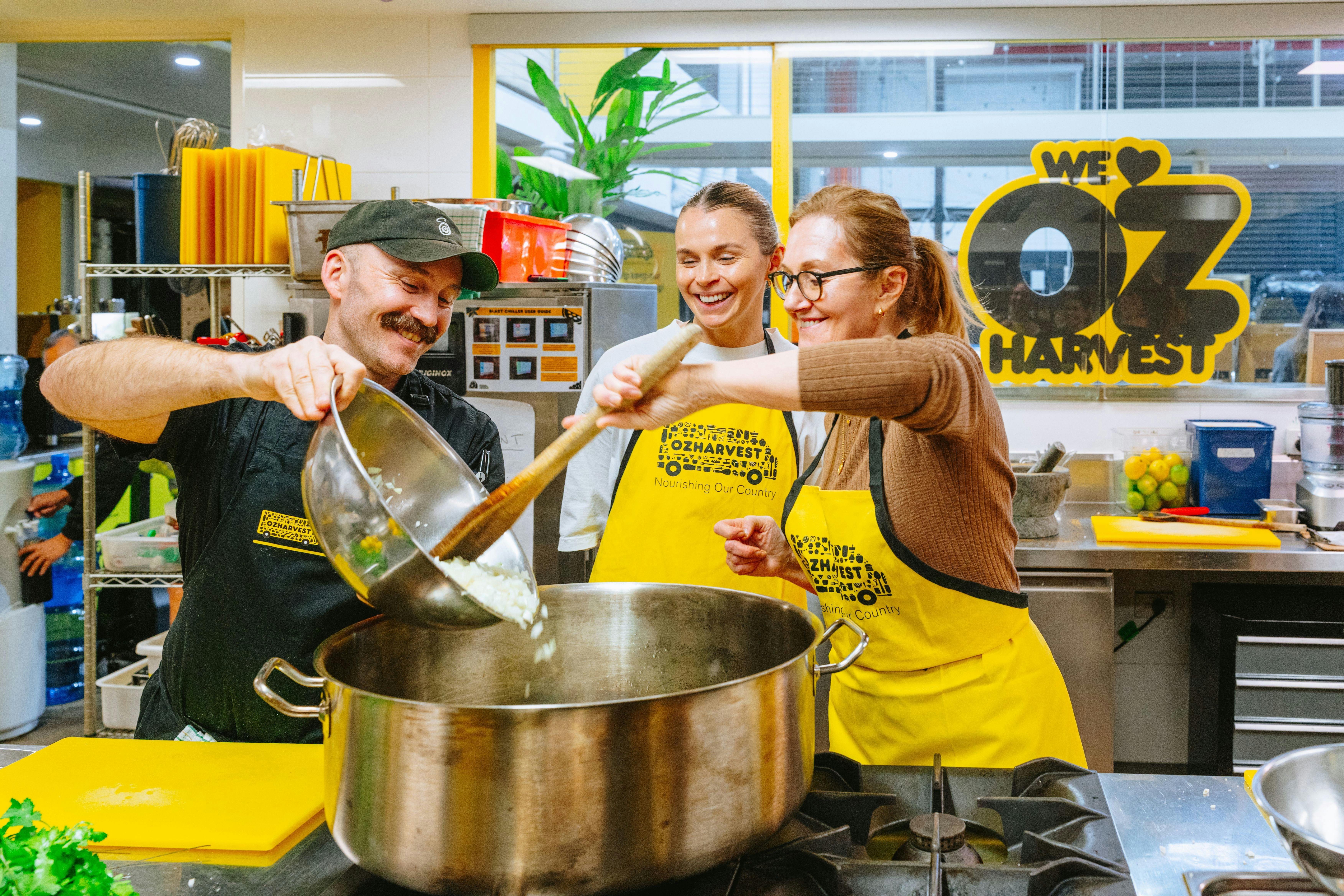 A chef leading a Cooking for a Cause Social cooking class, adding onion to a pot while two participa