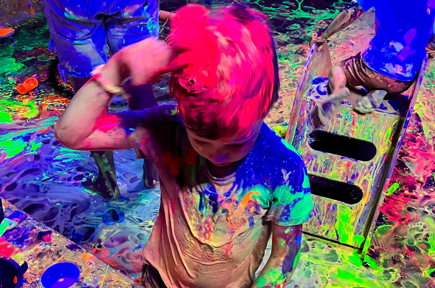 A child painting his hair with glowing red paint at Messy Glow Co UV Paint Room