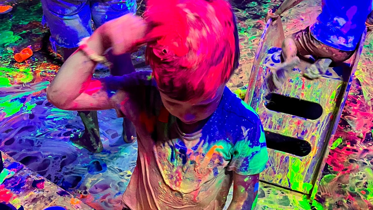 A child painting his hair with glowing red paint at Messy Glow Co UV Paint Room