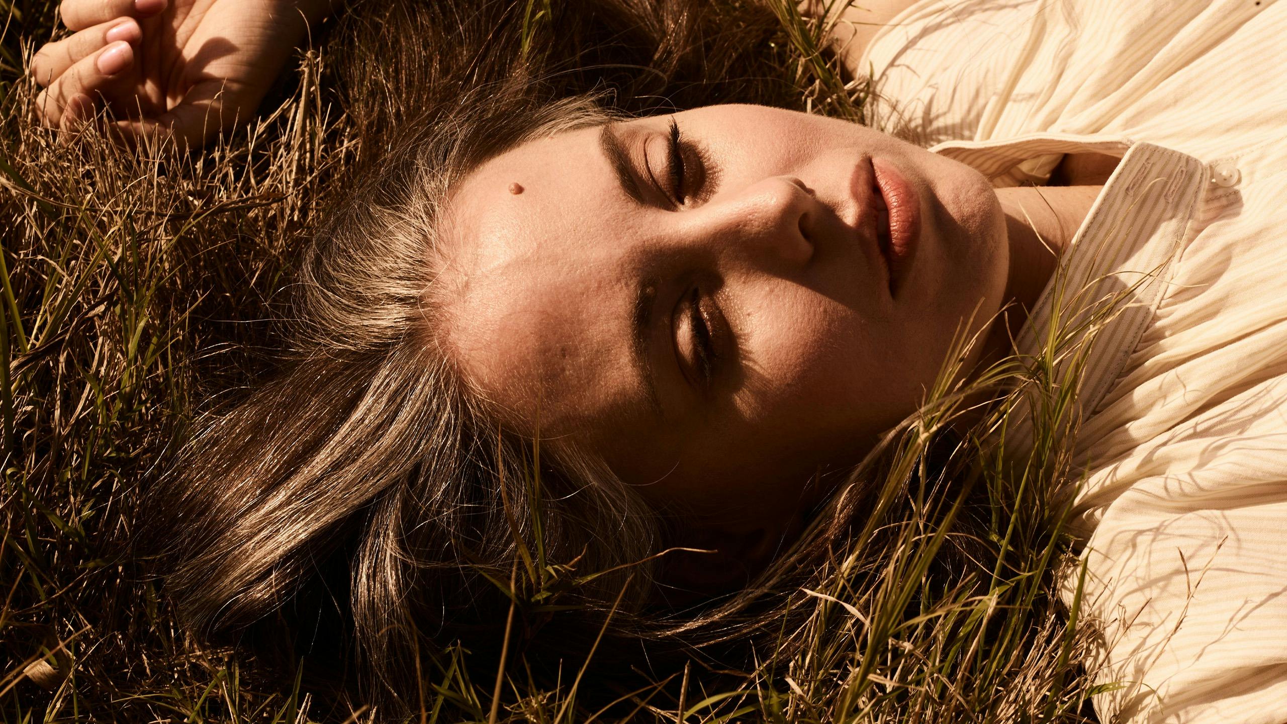 A woman lies in the dry grass with the sun on her face