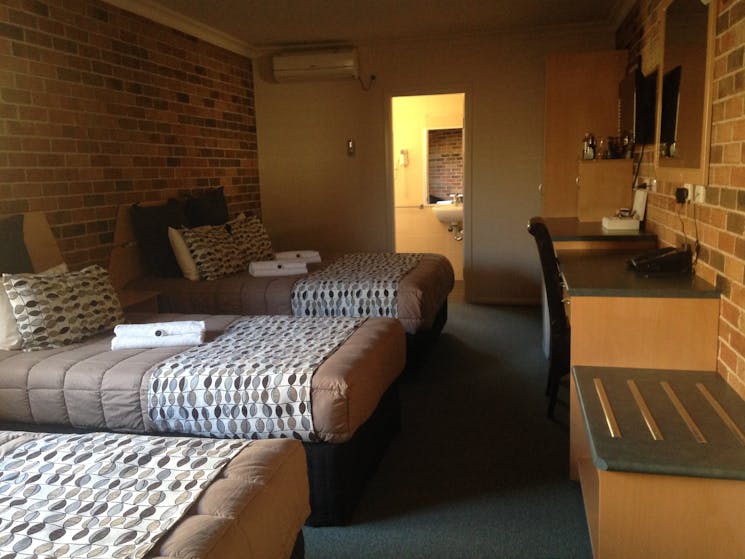 Three beds on left, bathroom door in background. Desk and supples on right.