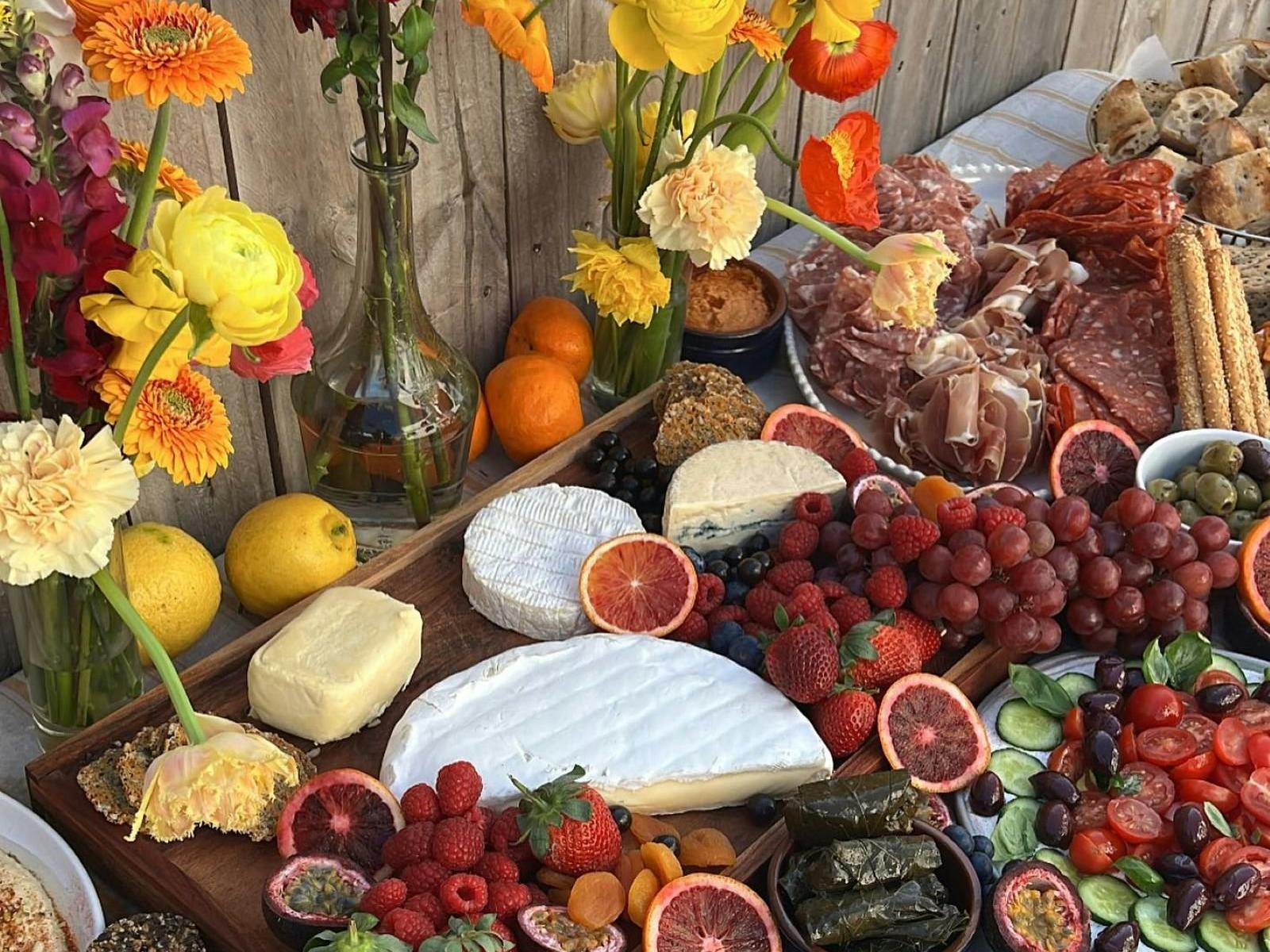 beautiful food platter including fruits, cheese wheels, dolmades, olives, meats, salads and flowers