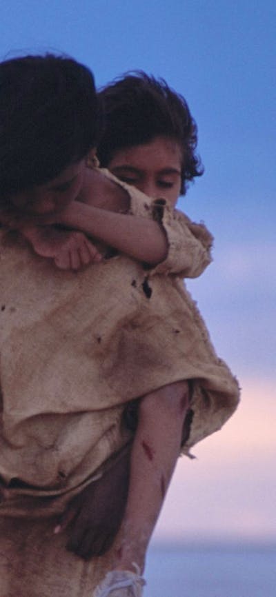 One young person piggy backs a younger person in a desolate setting