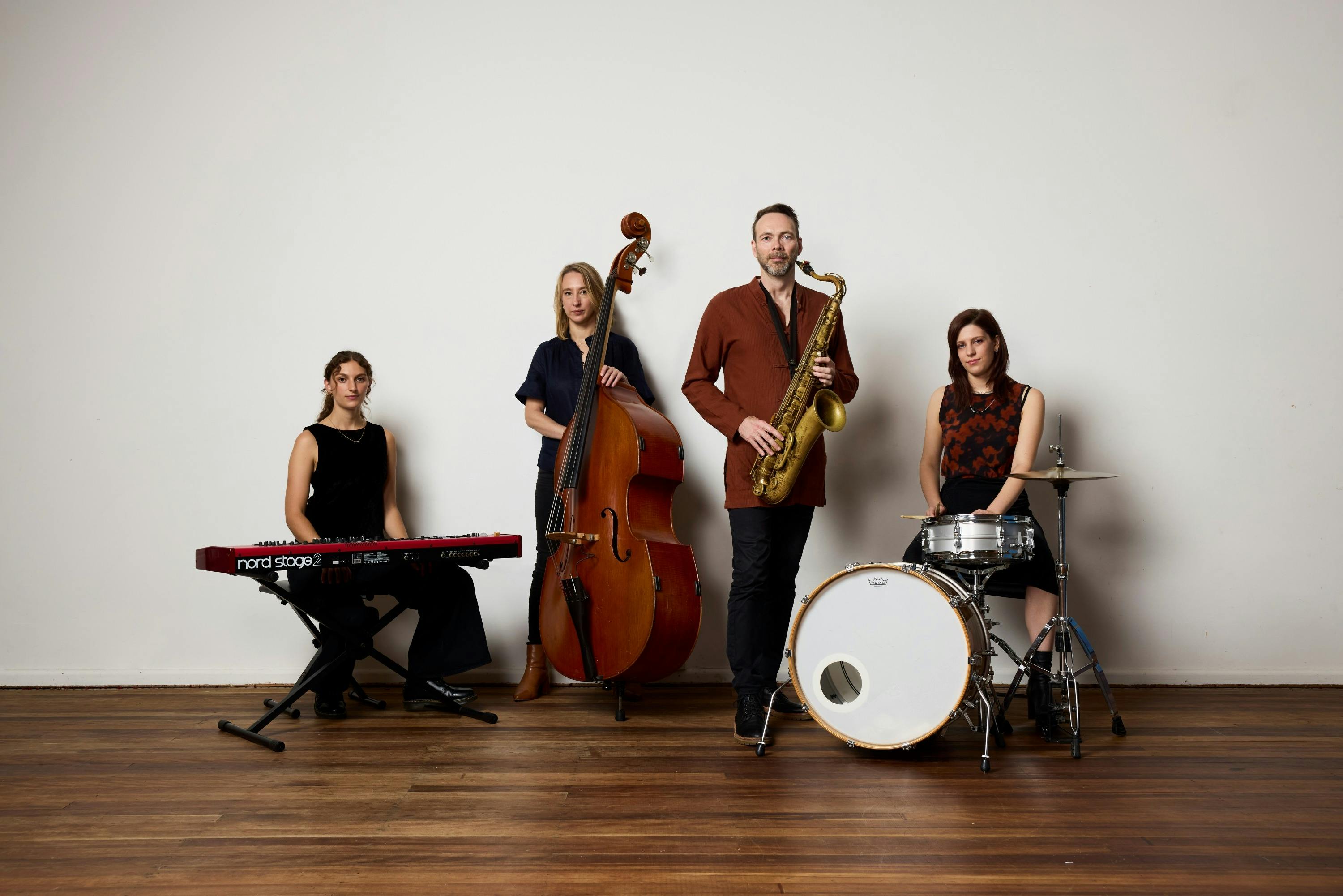 Four Musicians standing in front of white wall, holding instruments.