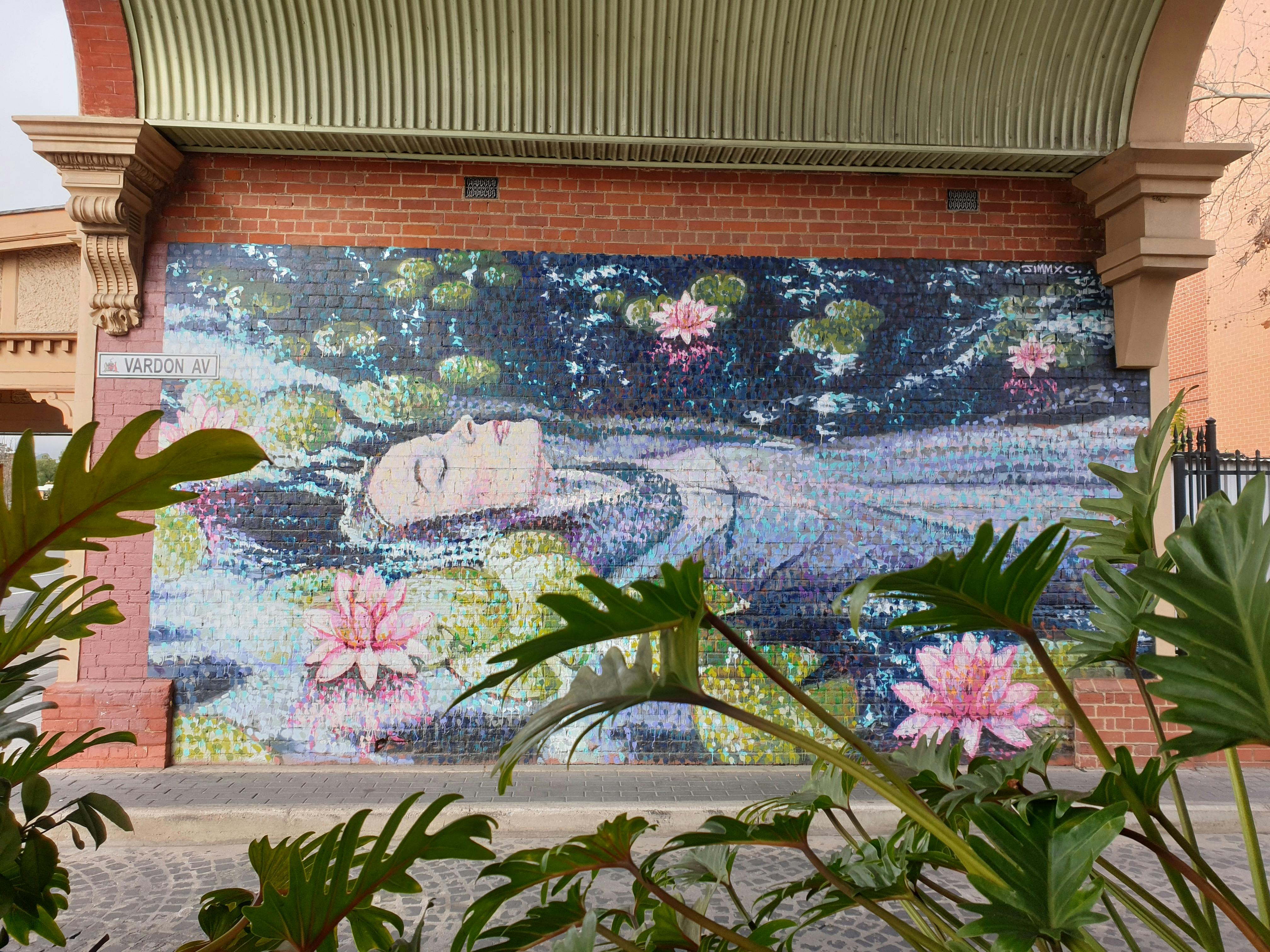 Street art by Jimmy C of a woman floating in a pond, framed by plants.