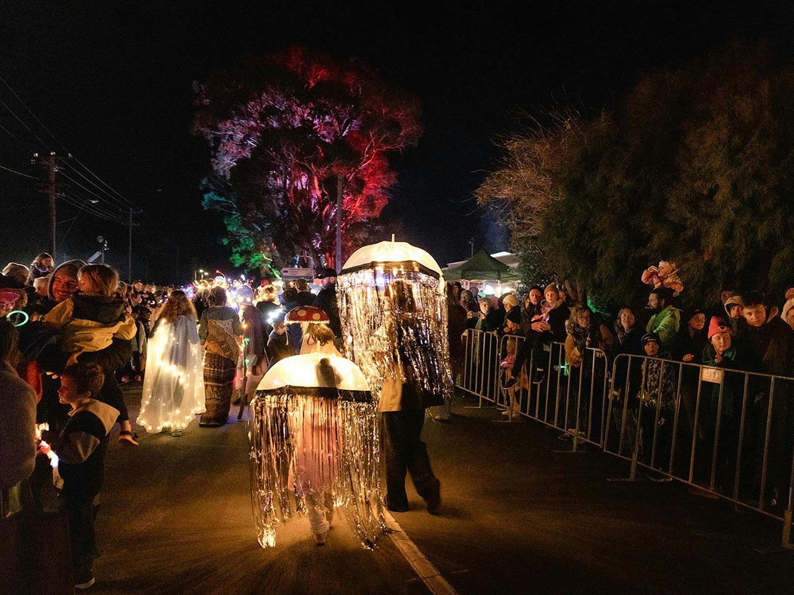 People in jelly fish umbrella costume walk up a street with many people watching on the sides.