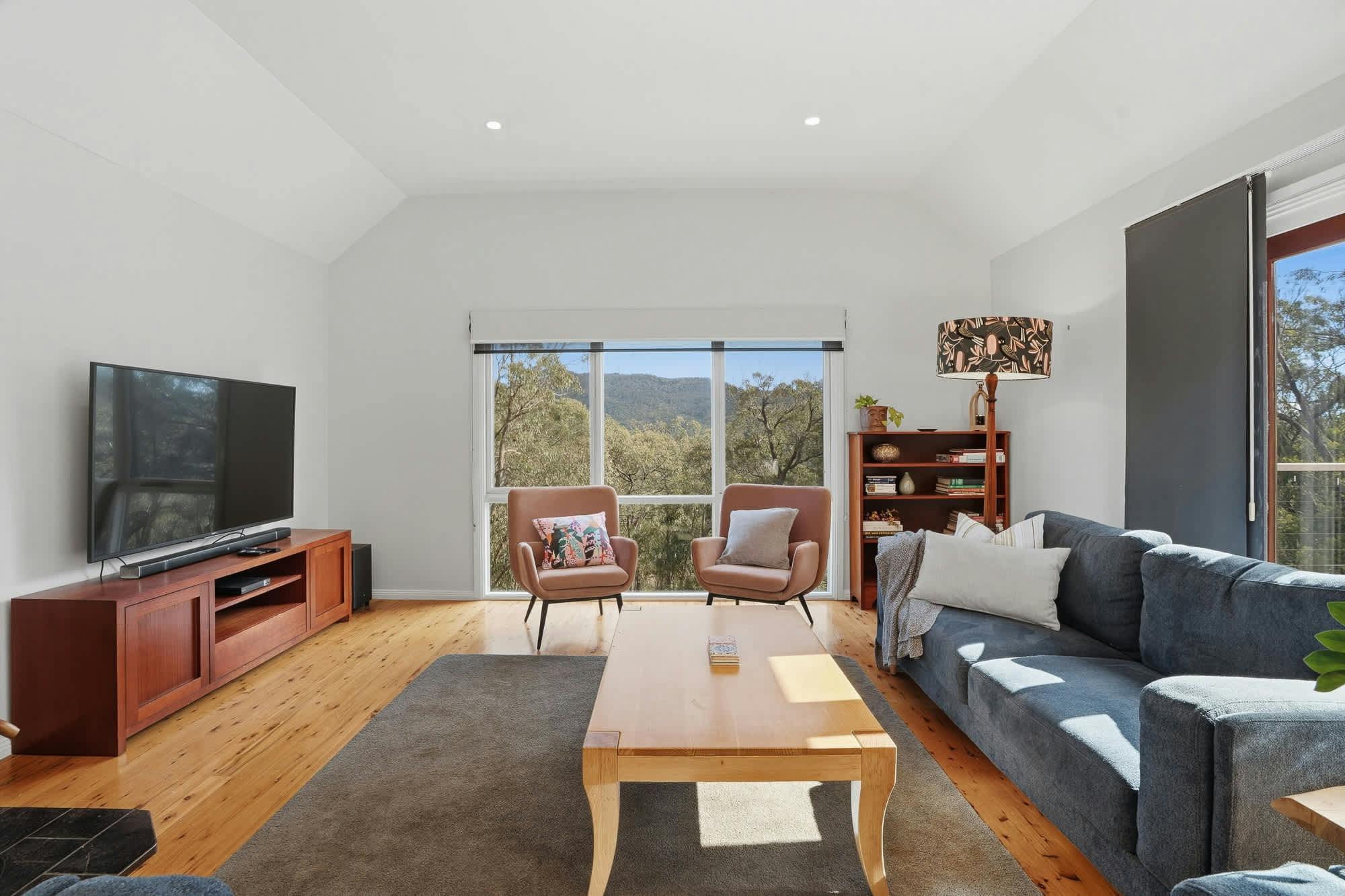 Large living area with arm chairs, couches, tv, coffee table, large window and rug