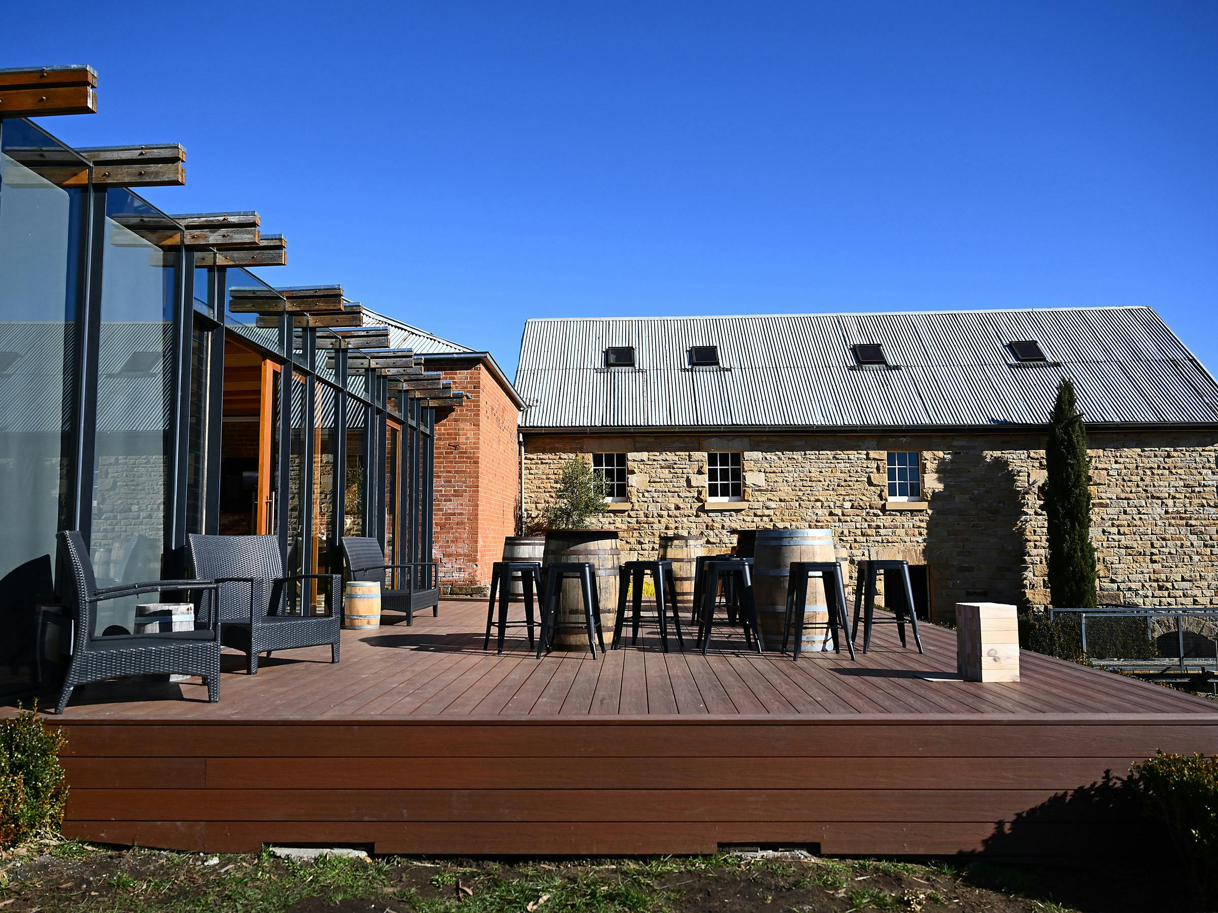 Outdoor deck with chairs, barrel tables and stone buildings at Clyde Mill.