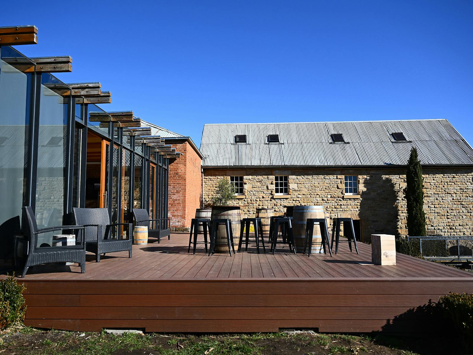 Outdoor deck with chairs, barrel tables and stone buildings at Clyde Mill.