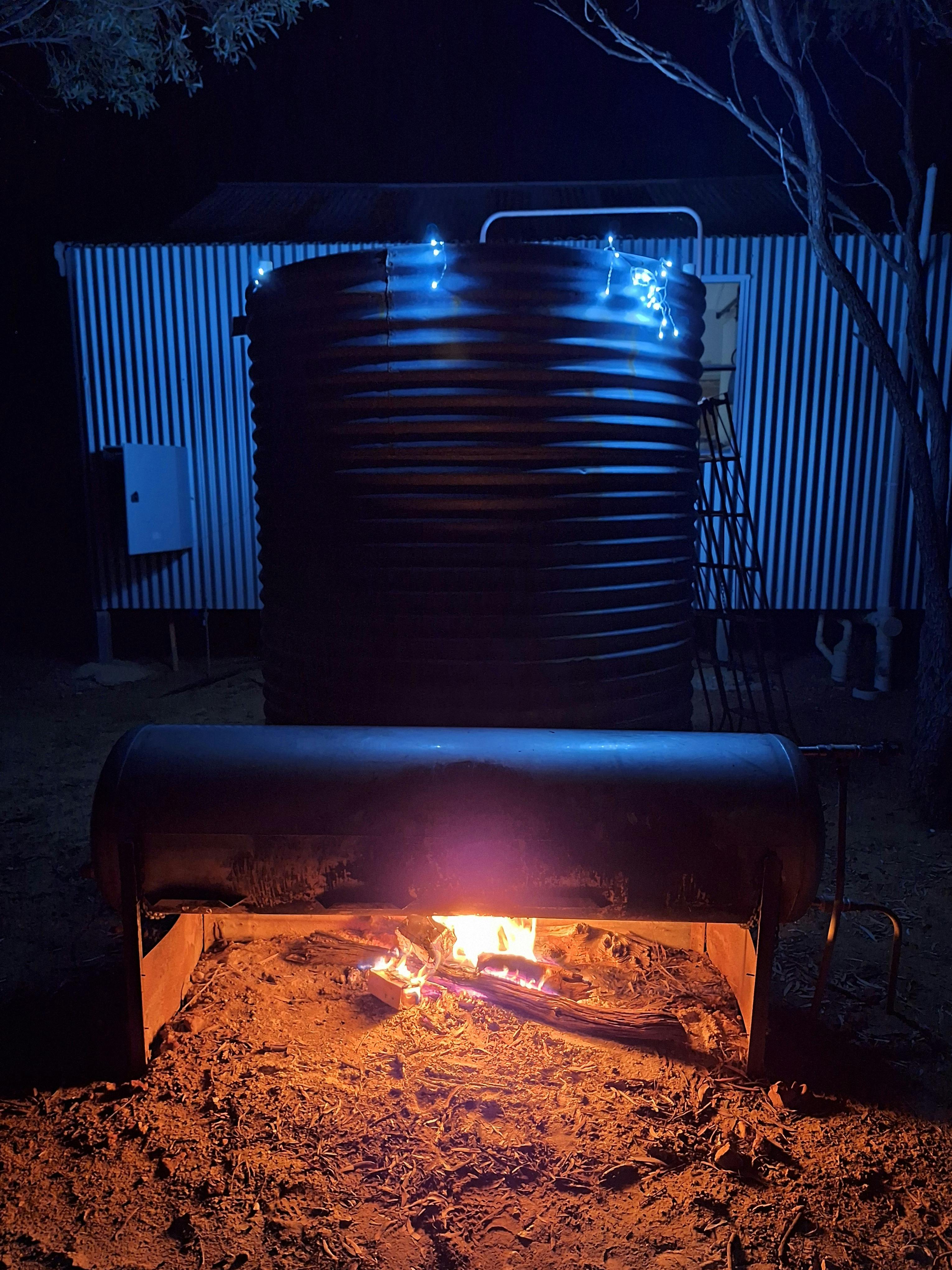 A corrugated iron shower with a tank of water being heated by a fire