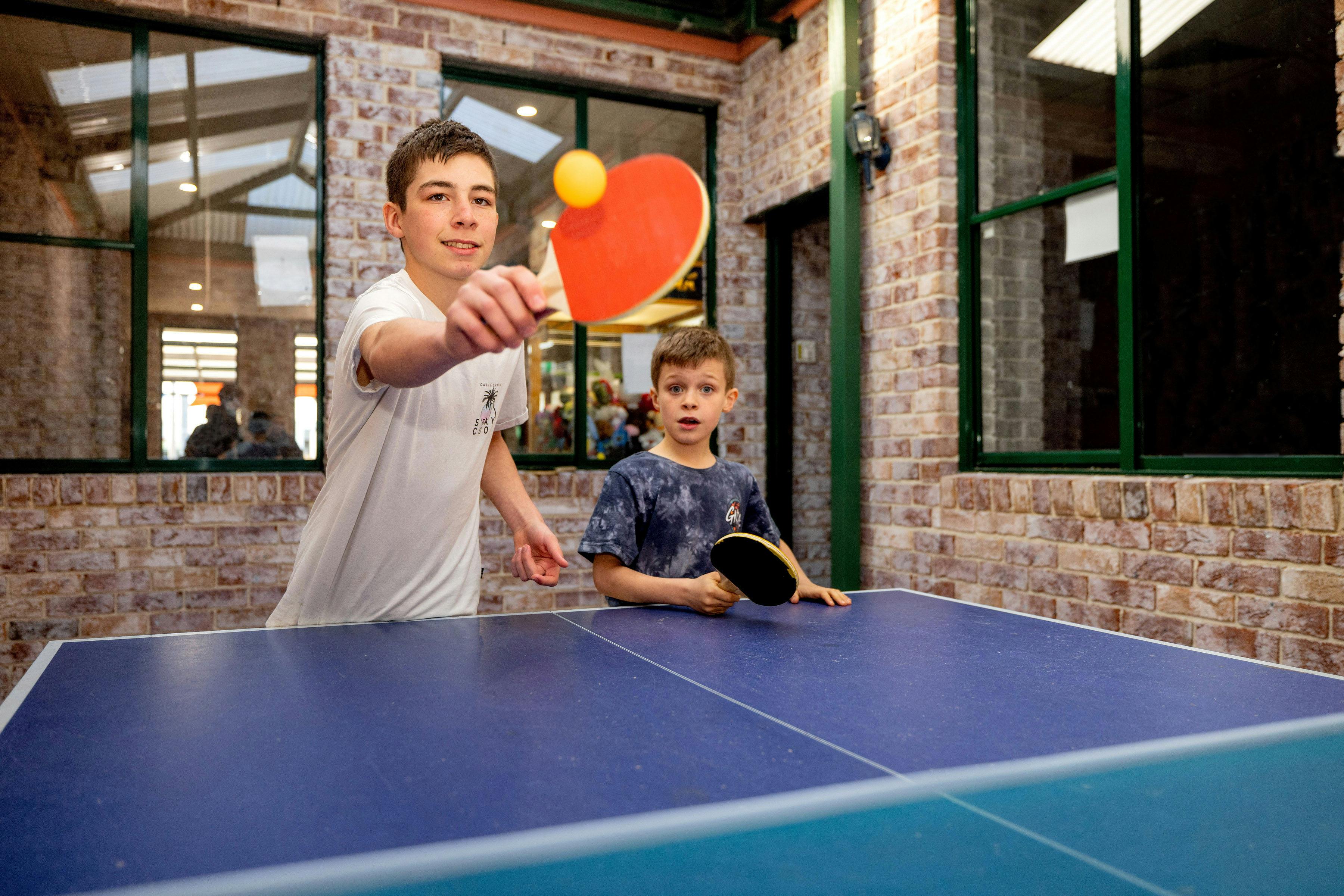 Two young boys standing in front of a blue table tennis table.