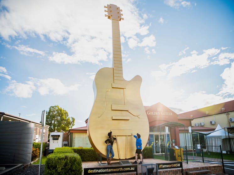 Photo of the Big Golden Guitar with 2 people in cowboy hats and boots looking up at it