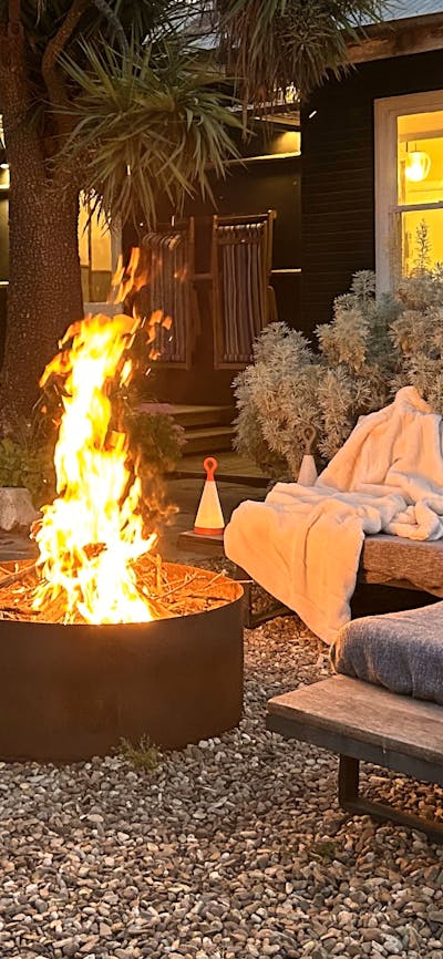 Firepit at dusk with outdoor couch, house in the background with lights on.