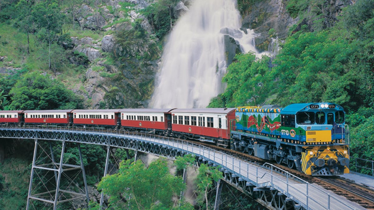 Aerial view of the Kuranda Scenic Railway train passing a waterfall along the cliff and rainforest