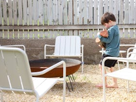 Outdoor fire pit surrounded by chairs on a gravel area beside a timber fence.