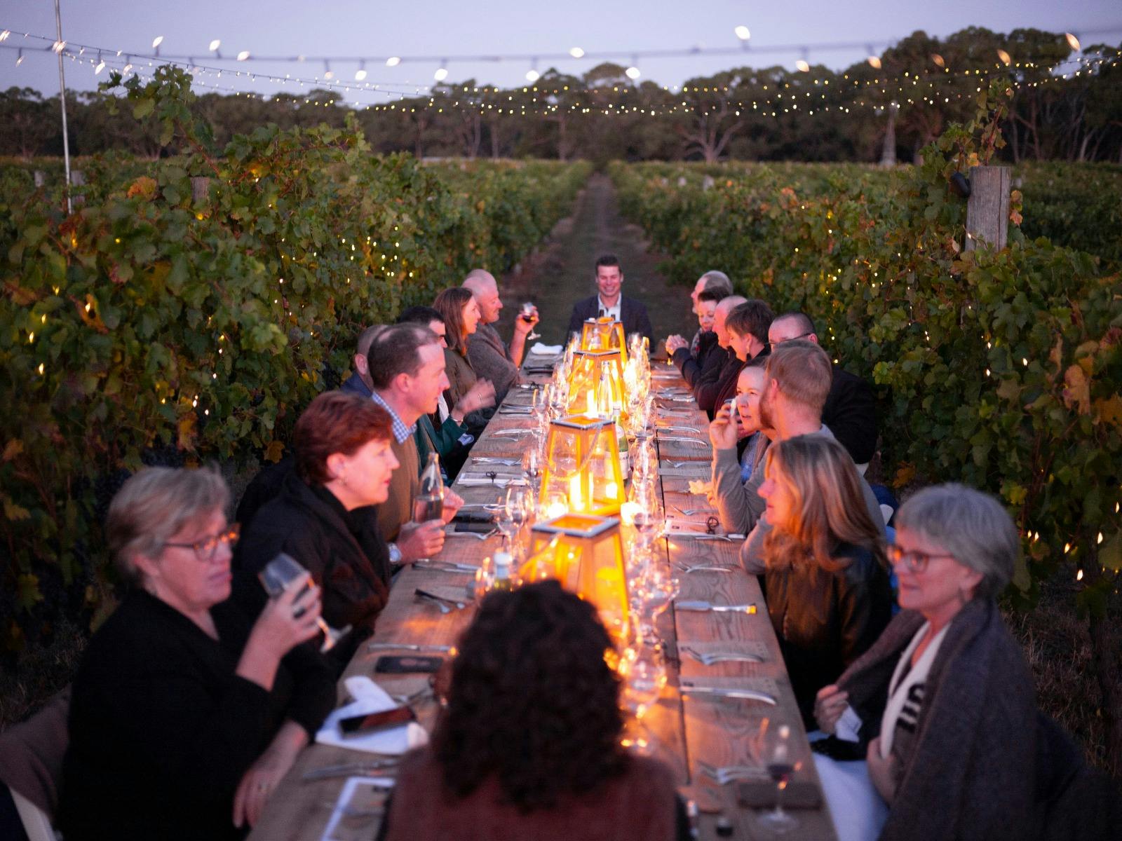 A table of people enjoying food & wine with candles under the night sky