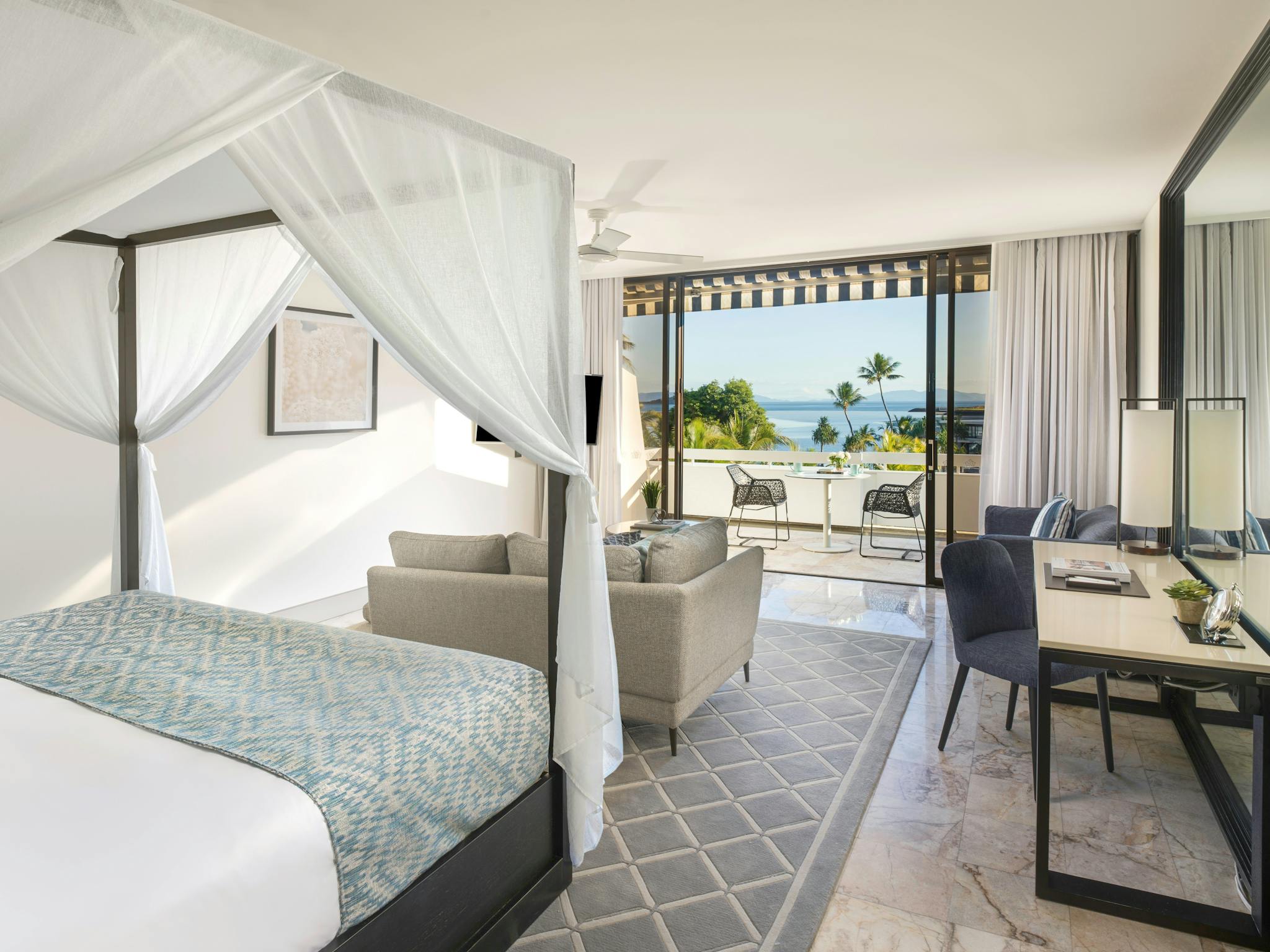 Modern room featuring a four-poster bed, sitting area, work desk, and balcony overlooking the ocean. Modern room featuring a four-poster bed, sitting area, work desk, and balcony overlooking the ocean.