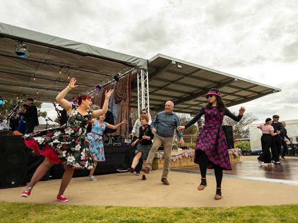 Group of dancers near stage kicking leg and arms in the air.
