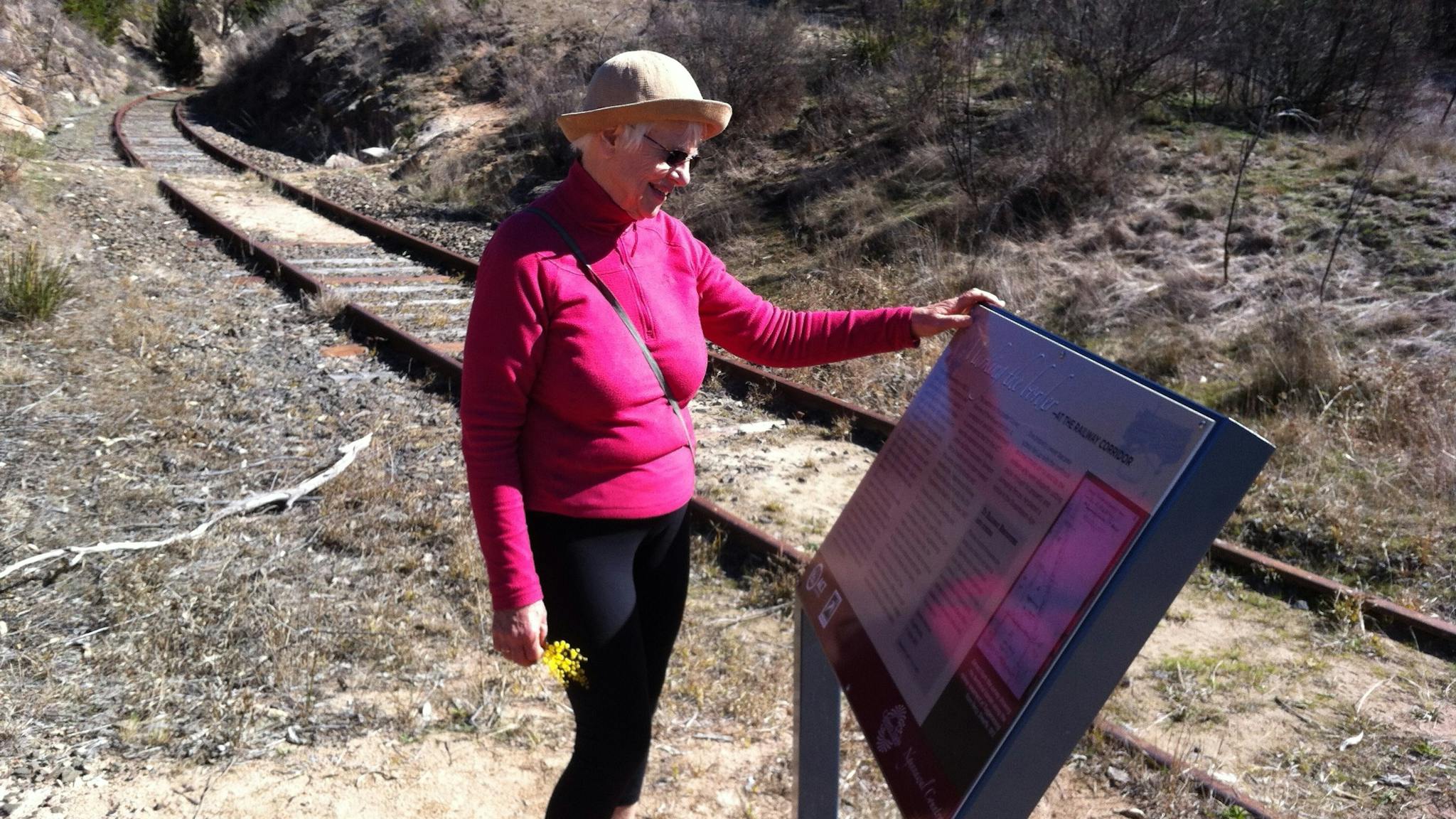 Woman reading sign board next to rail tracks