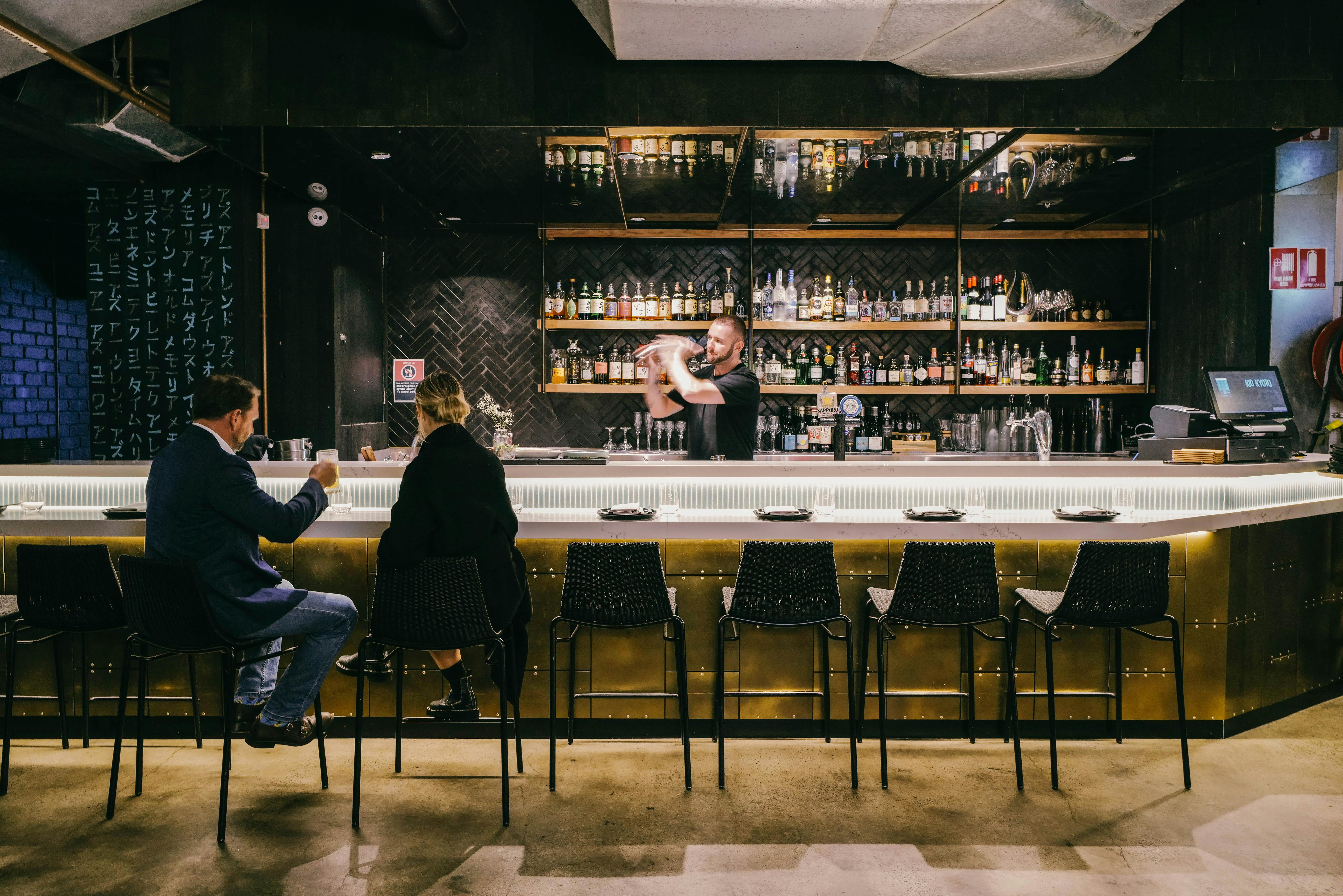 Customers having drinks at the bar whilst a bartender shake a cocktail