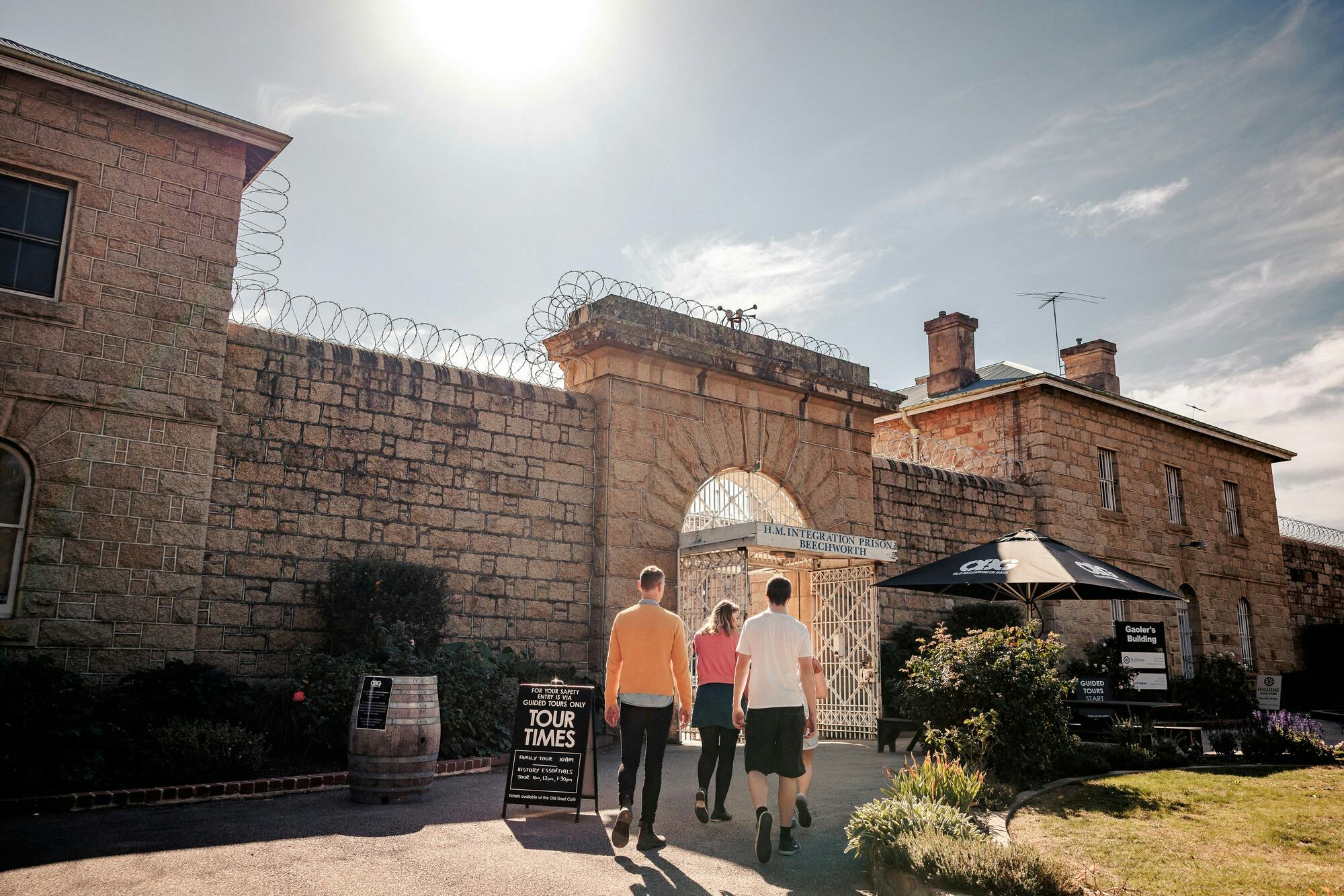 A family entering a large granite building with razor wire and a sign saying Old Beechworth Gaol