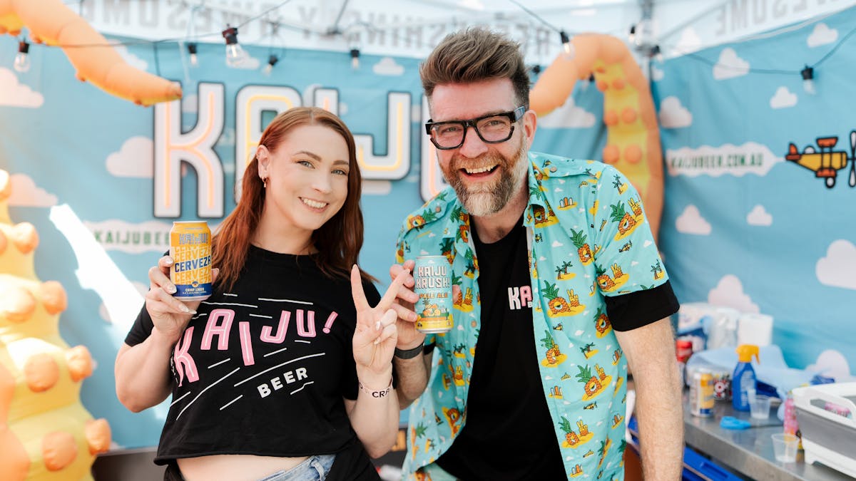 Woman and man working at a brewery stall holding a can smiling at the camera