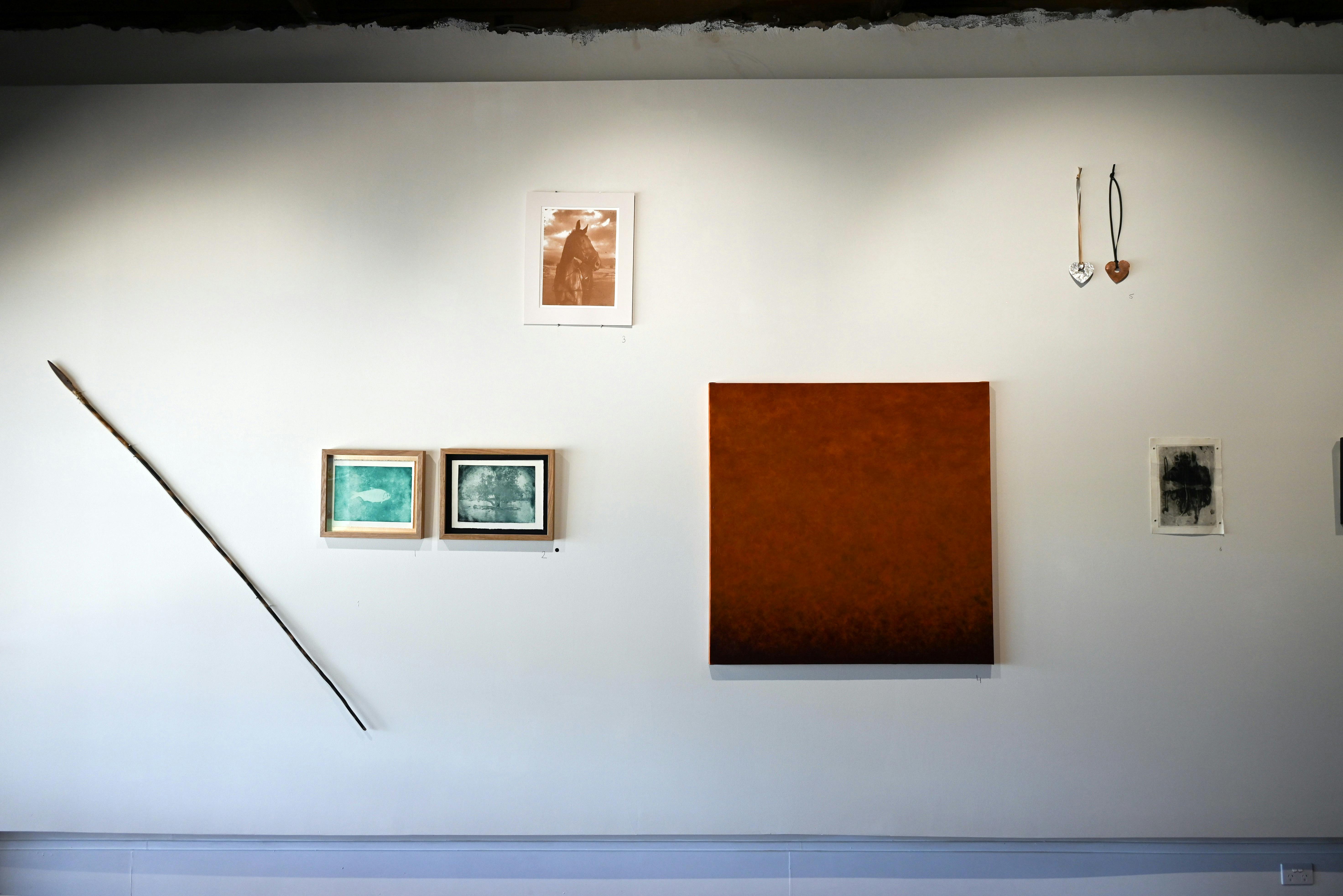 A series of sculptures, framed photos, paintings and jewellery are hung randomly on a white wall