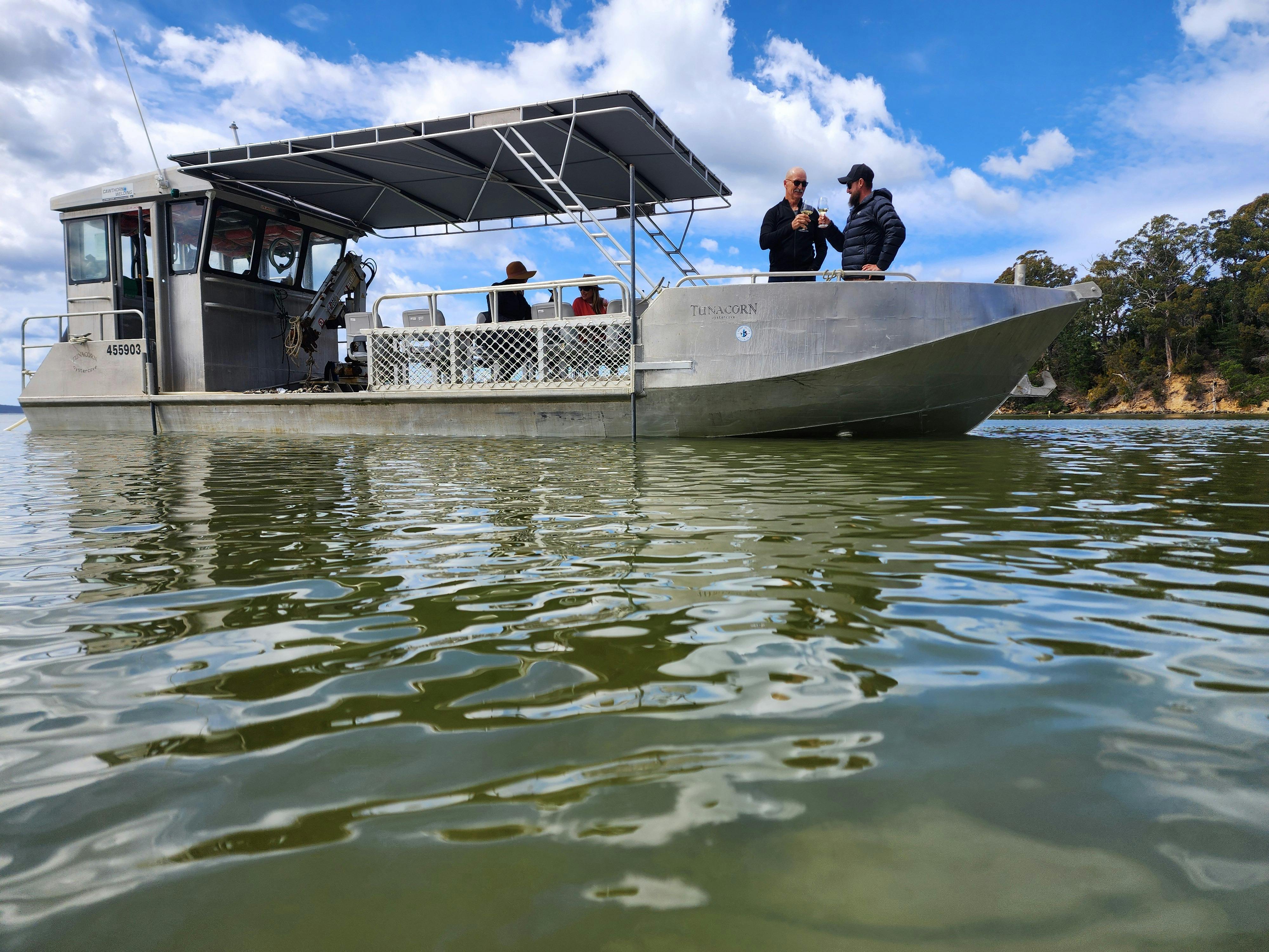 Boat glides on water with guests holding wine, shaded deck, leafy shoreline backdrop