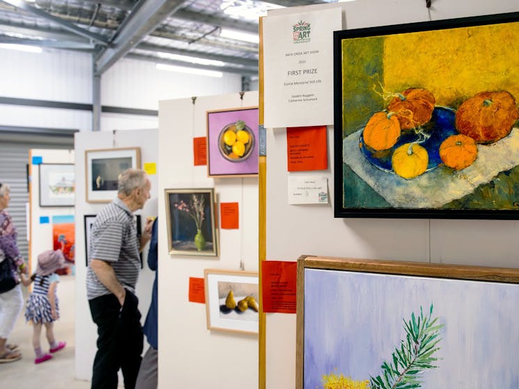 Foreground is a painting of pumpkins and a First Prize certificate; background is art show hanging