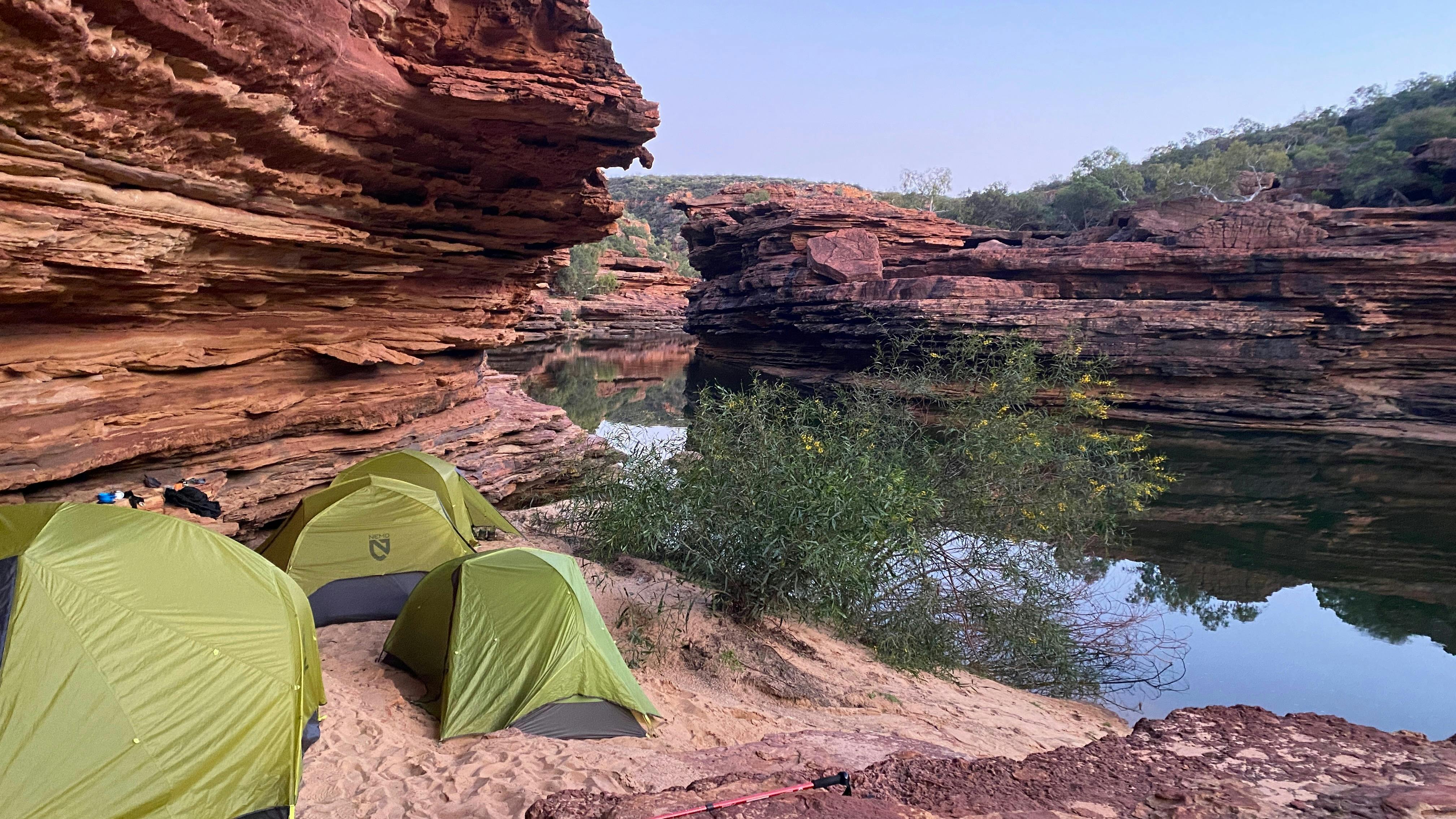 Green lightweight tents pitched close to the river's edge - red sandstone gorge walls around