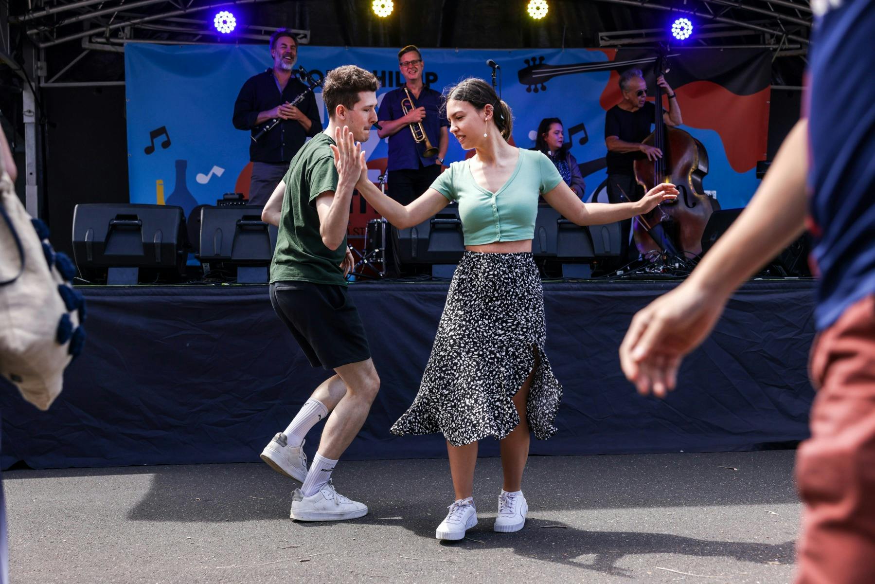 Two people dancing in front of a stage where a band is performing, surrounded by other attendees.