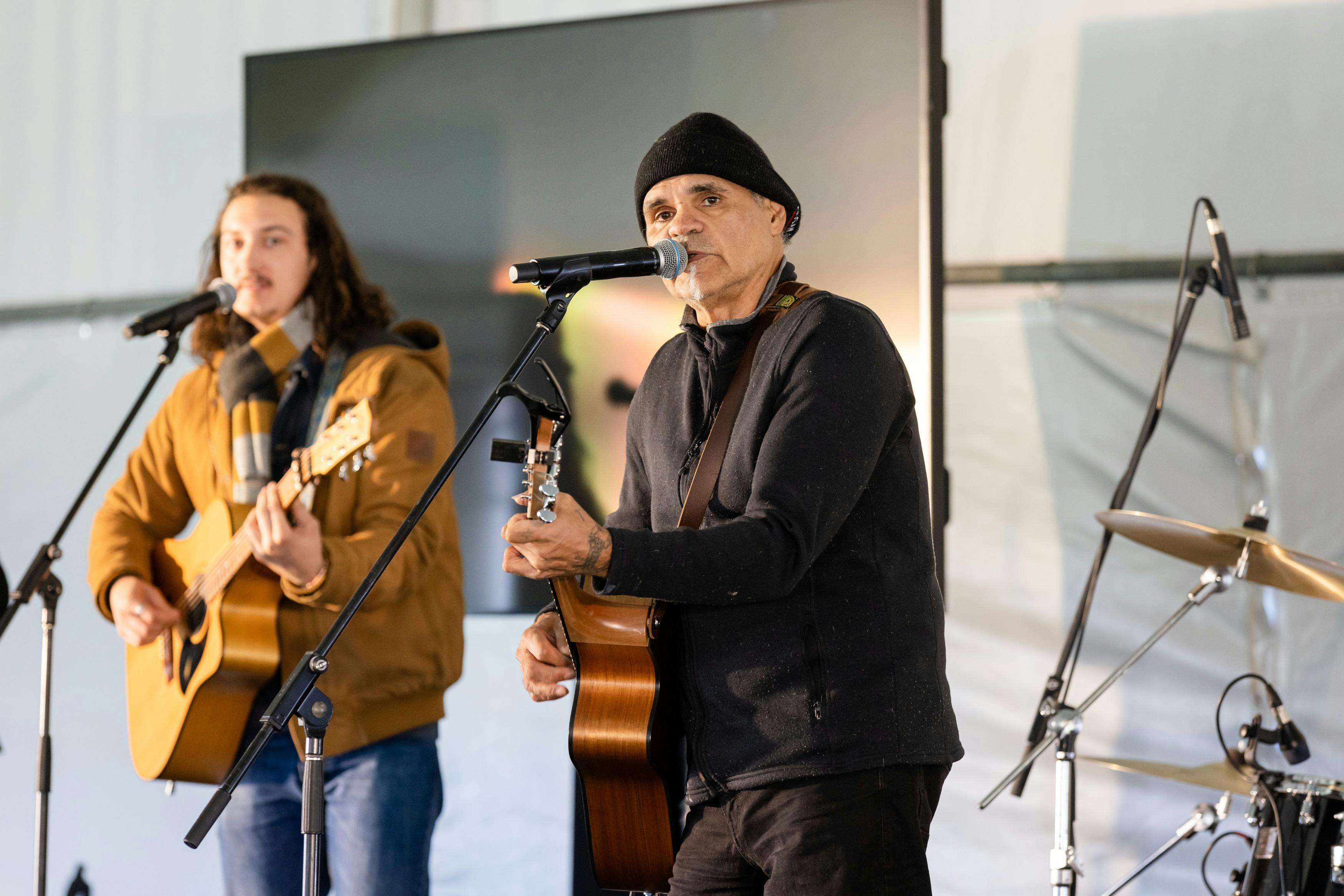 Two individuals playing acoustic guitars and singing into microphones on stage