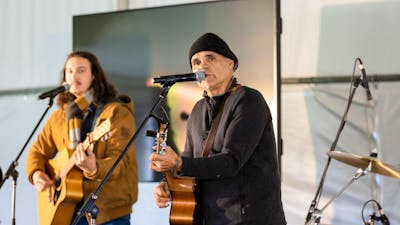 Two individuals playing acoustic guitars and singing into microphones on stage