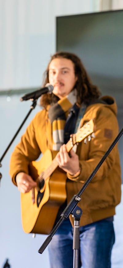 Two individuals playing acoustic guitars and singing into microphones on stage