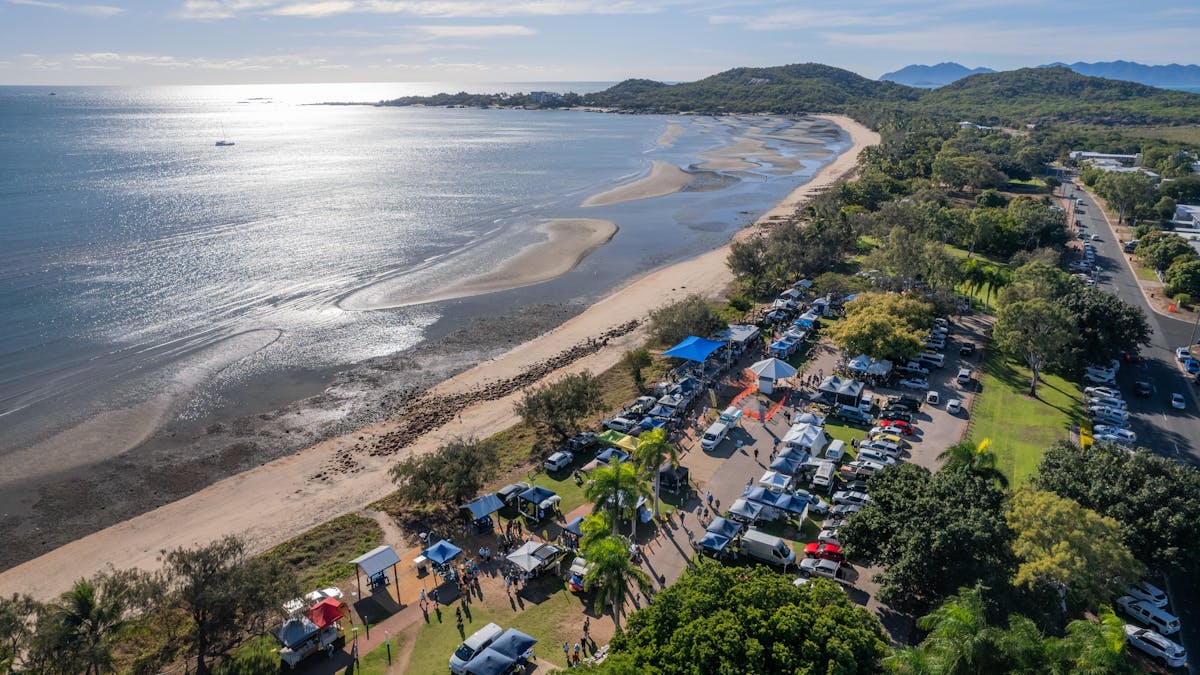 Aerial view of the market stalls and cars along a beautiful beach, greenery and calm ocean waters
